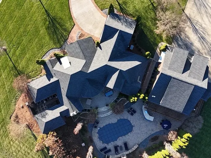 Aerial view of a dark shingle roof replacement over a home with a pool