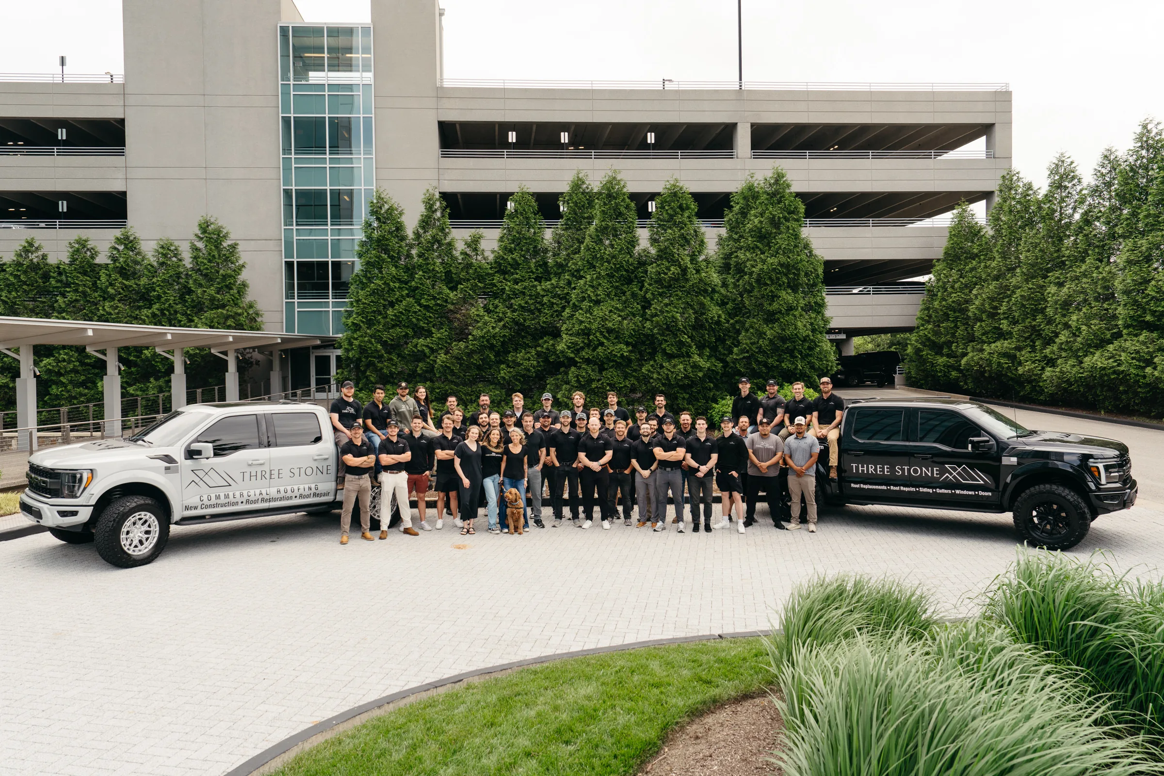 The Three Stone team gathered between two company trucks outside the office